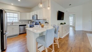 A modern kitchen with white cabinetry, a central island with bar stools, a microwave, and a flat-screen TV mounted on the wall. - FREE GOLF CART. private HEATED pool option. Walk to the beach.Sleeps 10! (Destin)