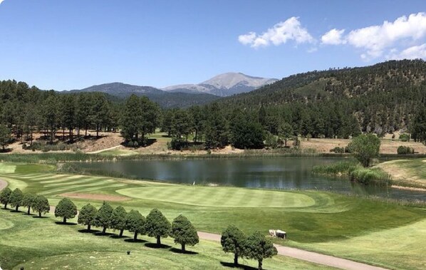 A golf course with a lake, trees, and a mountain in the background.