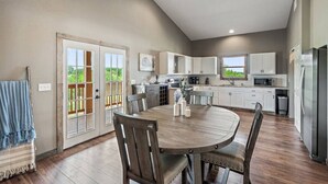 A modern kitchen with white cabinets, a dining table with chairs, and a view of greenery through the sliding glass doors. - ** NEW 5 STAR HILL COUNTRY RETREAT ** (Dripping Springs)