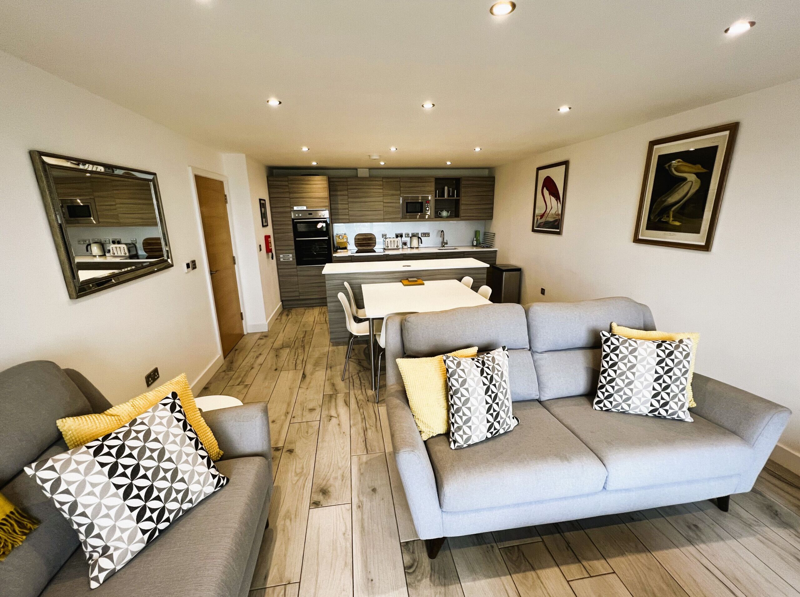 A modern living room with a grey sofa, a dining table, and a kitchen in the background.