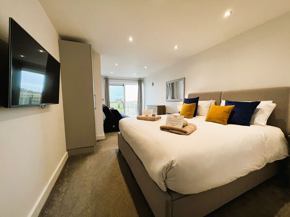 A modern hotel room with a large bed, a flat-screen TV, and a view of the outdoors.