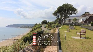 Une propriété située sur la côte, avec vue sur la plage, un phare et un espace verdoyant agrémenté d’un banc.