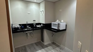 A modern kitchen with a black countertop, white appliances, and a wooden floor. - Cozy apartment with modern design - Sol Alphaville Hotel & Residence (Barueri)