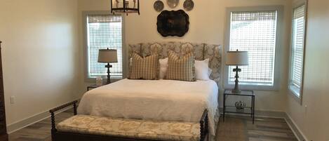 A bedroom with a large bed, a bench, two bedside tables with lamps, and a chandelier.