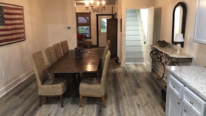 A dining area with a long wooden table and woven chairs, a chandelier, and a kitchen area with white cabinets and a granite countertop. - SunShiner Farm - Shiner, TX (Shiner)