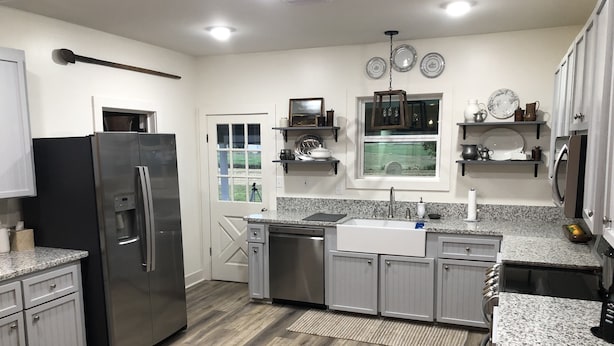 A modern kitchen with a stainless steel refrigerator, granite countertops, and wooden flooring. - SunShiner Farm - Shiner, TX (Shiner)