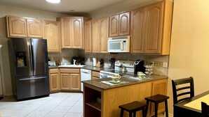 A kitchen with wooden cabinets, a stainless steel refrigerator, a microwave, a stove, and a dining area with stools.