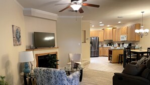 A modern living room with a fireplace, a television, and a dining area with wooden cabinets and a refrigerator.