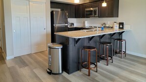Eine moderne Küche mit dunklen Schränken, Edelstahlgeräten, einer Granitarbeitsplatte und drei Barhocker.