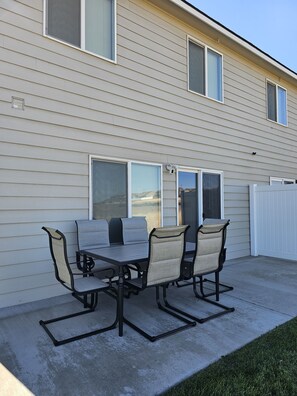 A patio with a table and chairs, a sliding glass door, and a white fence. - Downtown Hermiston (Hermiston)