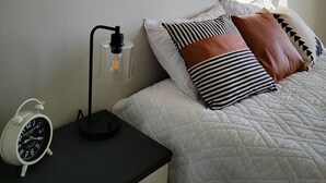A bedroom with a bed, a nightstand, a lamp, a clock, and two framed pictures on the wall. - Downtown Hermiston  (Hermiston)