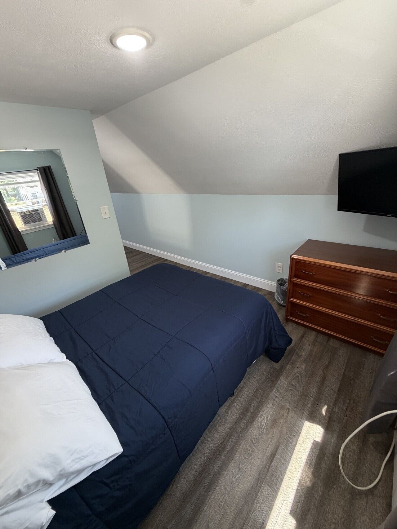 A bedroom with a bed, a dresser, a TV, and a window with curtains.