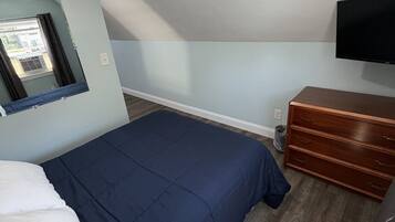 A bedroom with a bed, a dresser, a TV, and a window with curtains.