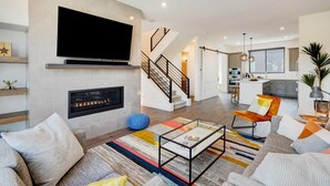 A modern living room with a fireplace, a TV, and a staircase leading to an upper level.