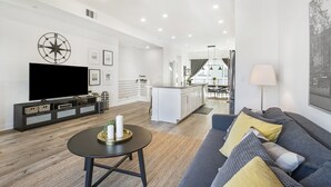 A modern living room with a flat-screen TV, a sofa, a coffee table, and a kitchen area in the background. - LA Harbor View with Private Rooftop and FREE Tesla Charger (San Pedro)