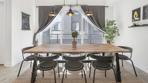 A dining area with a wooden table, black chairs, a potted plant, and a view of the city through large windows. - LA Harbor View with Private Rooftop and FREE Tesla Charger (San Pedro)