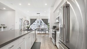 A modern kitchen with stainless steel appliances, a central island, and a view to a dining area. - LA Harbor View with Private Rooftop and FREE Tesla Charger (San Pedro)