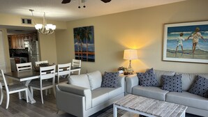 A living room with a sofa, coffee table, and dining area with chairs. - Updated condo just steps to the white sand beaches of Clearwater Beach (Clearwater)