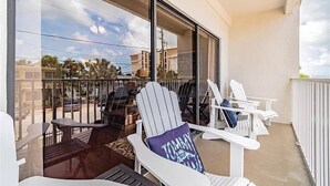 A balcony with white Adirondack chairs, a table, and a view of the street and buildings. - Updated condo just steps to the white sand beaches of Clearwater Beach (Clearwater)
