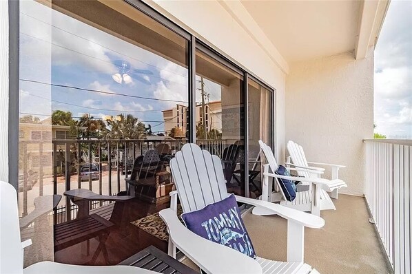 A balcony with white Adirondack chairs, a table, and a view of the street and buildings.