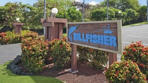 Et skilt for 'Billfisher' med et logo af en fisk og en båd, omgivet af røde blomster og grønt.