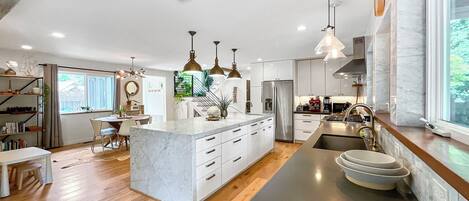 A modern kitchen with a marble island, stainless steel appliances, pendant lighting, and a view of the outdoors.