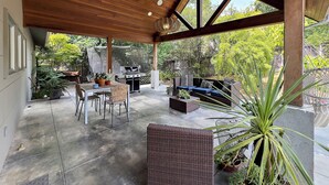 Un patio cubierto con techo de madera, mobiliario exterior, una parrilla y plantas en macetas.