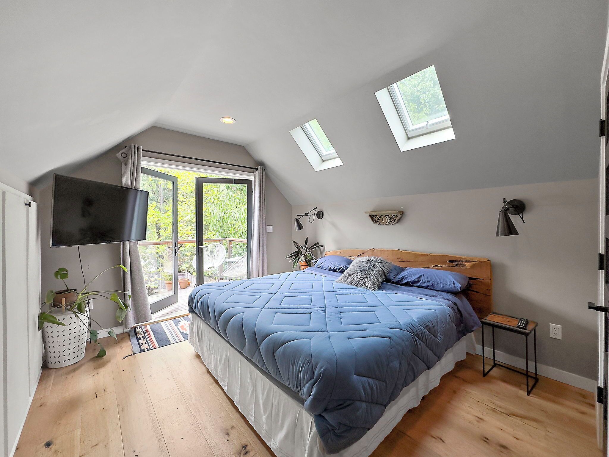 Une chambre avec un lit, une télévision, une petite table, une plante et un balcon avec vue.