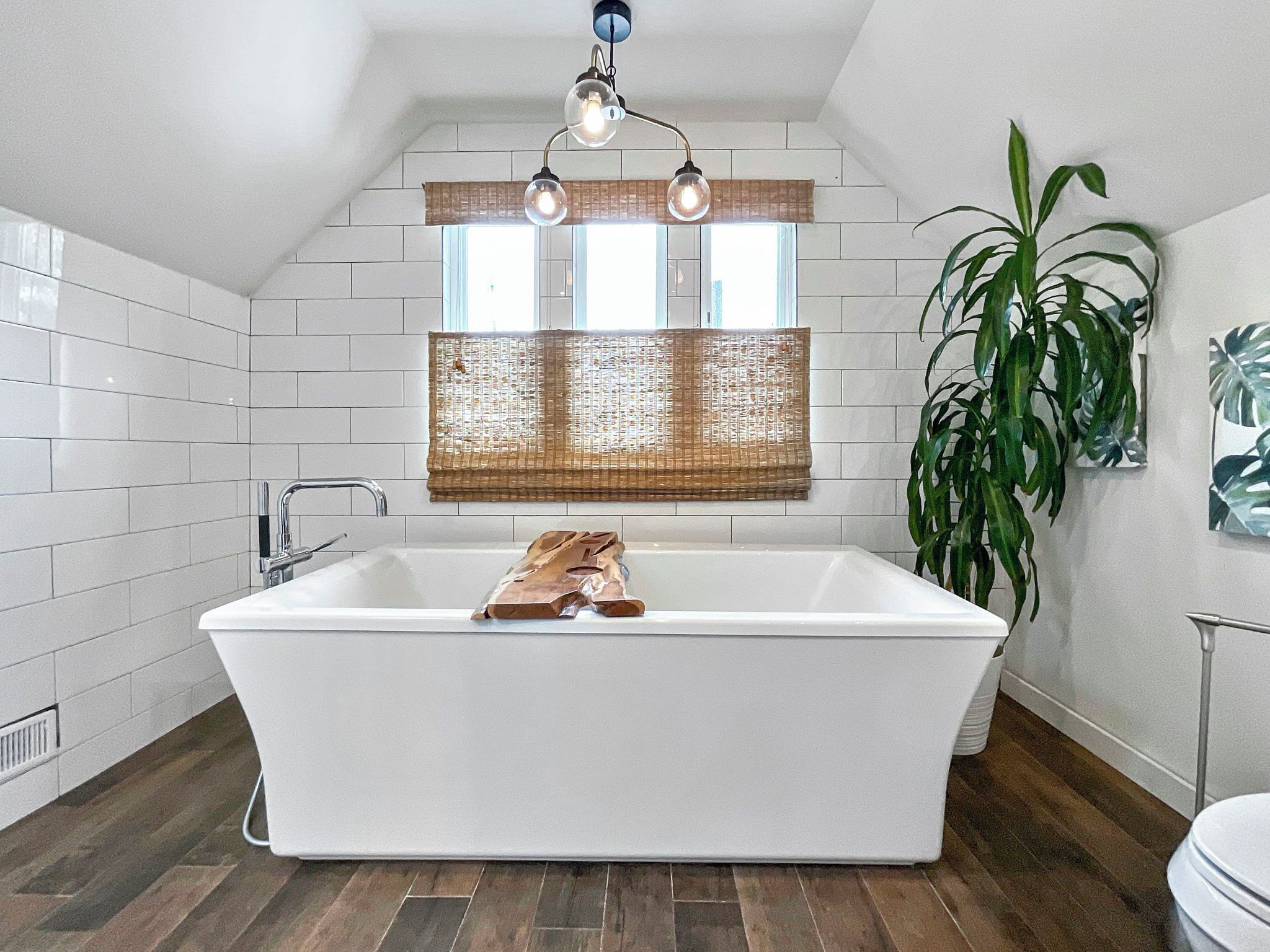 Un baño moderno con una bañera independiente, un ventanal con persiana de bambú y una planta en maceta.