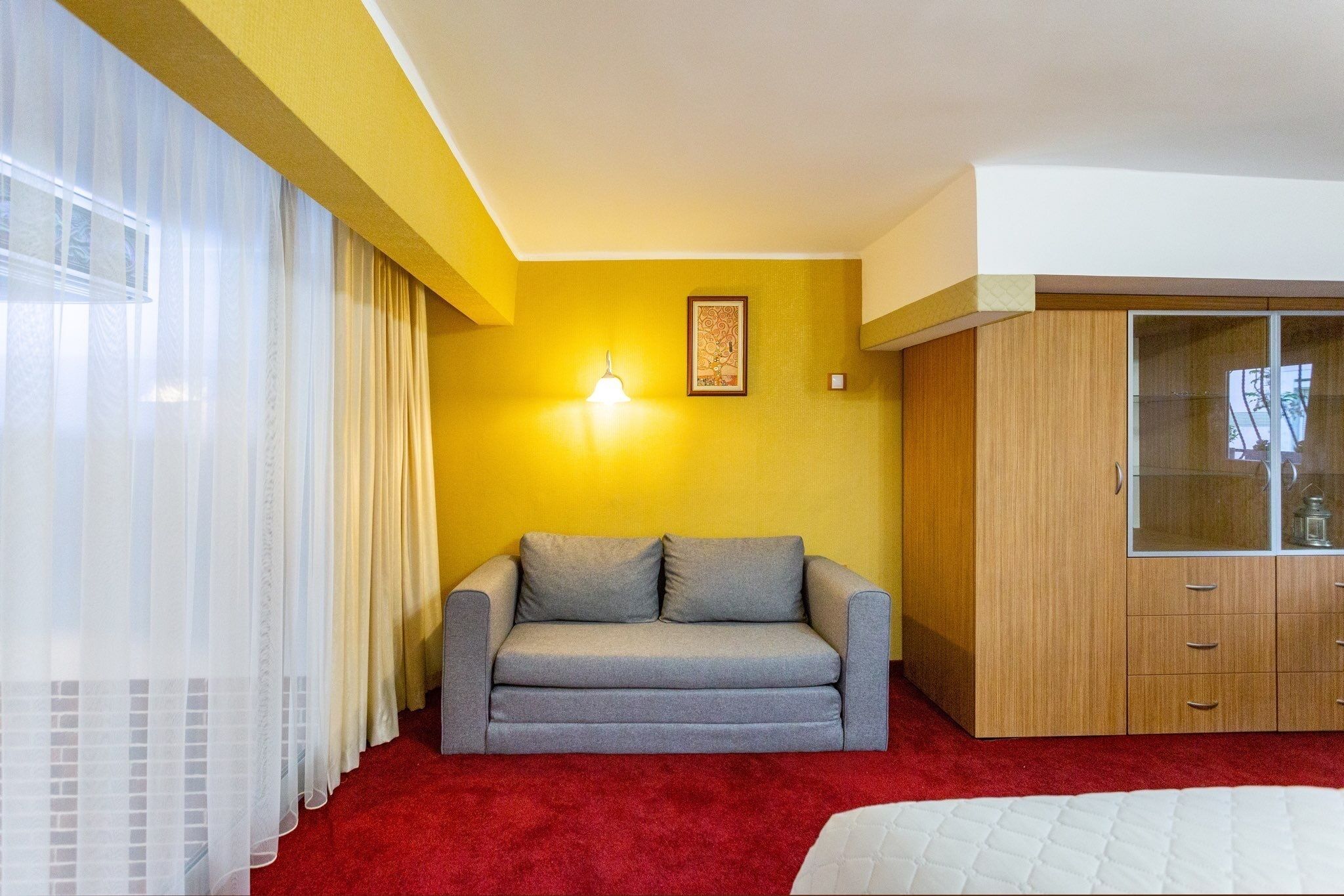 A room with a grey sofa, a wooden wardrobe, a red carpet, and a yellow wall.