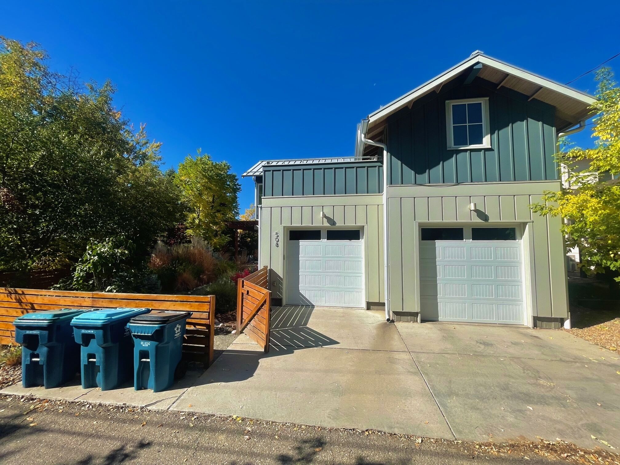 A two-story house with a garage, a front porch with wooden benches, and a clear blue sky.