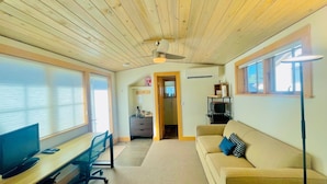 A room with a wooden ceiling, a desk with a computer, a couch, and a lamp.