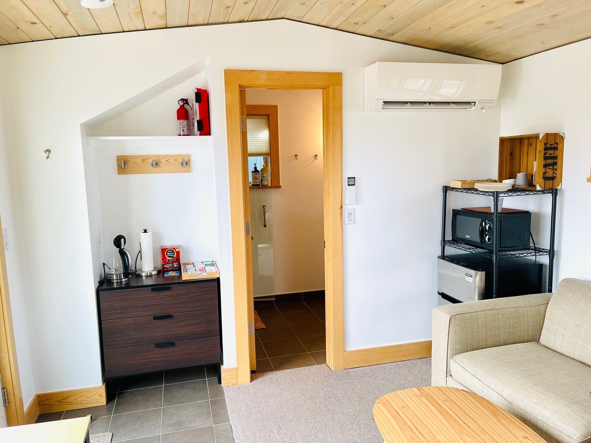 Un espacio habitable pequeño con kitchenette, sofá y techo de madera.