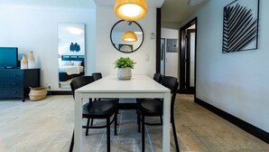 Un espace repas moderne avec une table blanche et des chaises noires, une plante en pot et un grand miroir au mur.