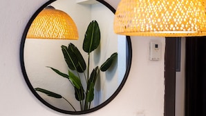 Un miroir rond avec un cadre noir, une plante en pot et deux lampes suspendues à la texture tissée.