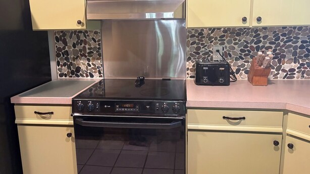 A kitchen with a stainless steel range hood, a built-in oven, a toaster, and a stone-patterned backsplash.