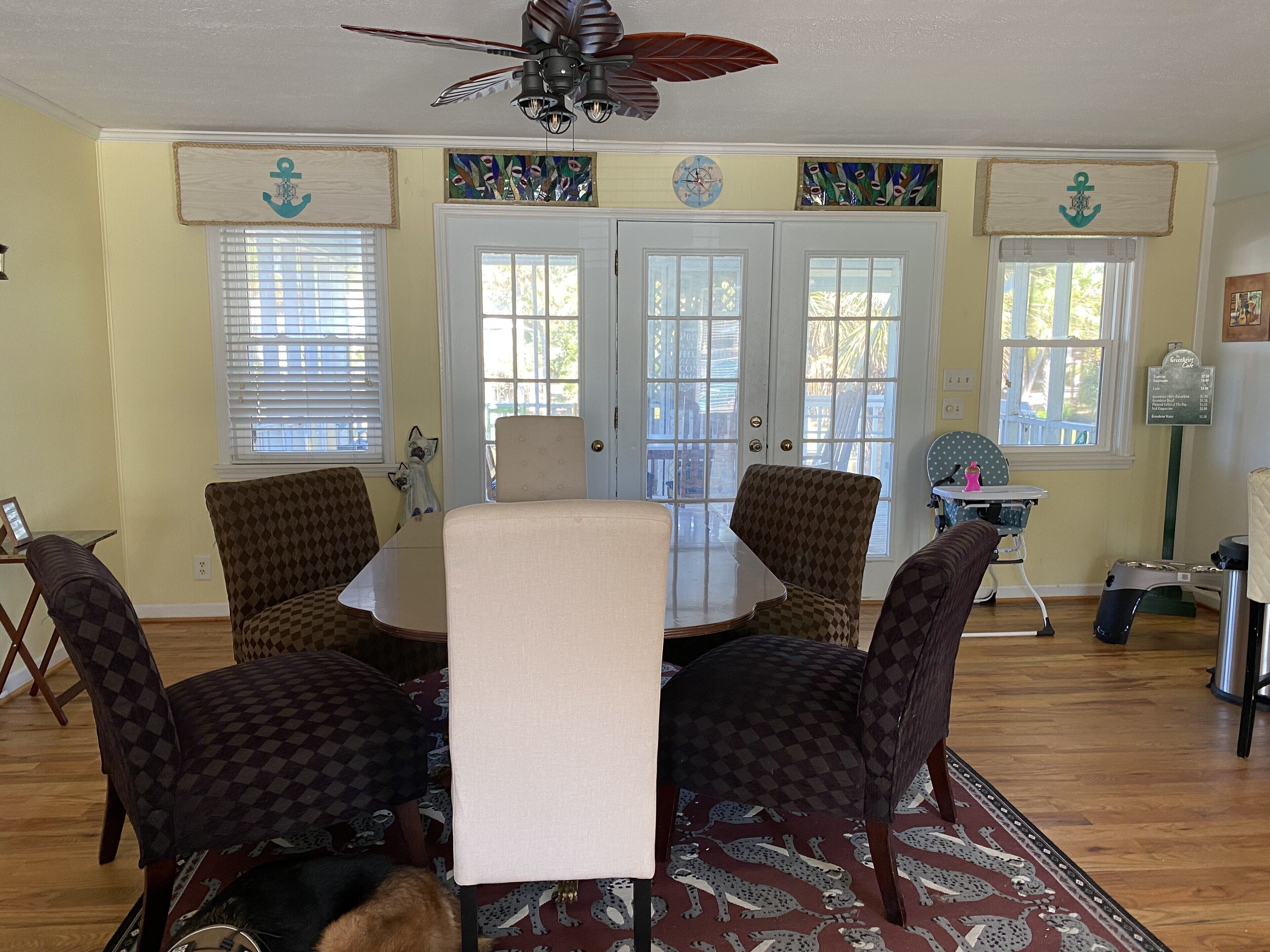 Un comedor con una mesa redonda y cuatro sillas estampadas, un ventilador de techo y decoración mural.