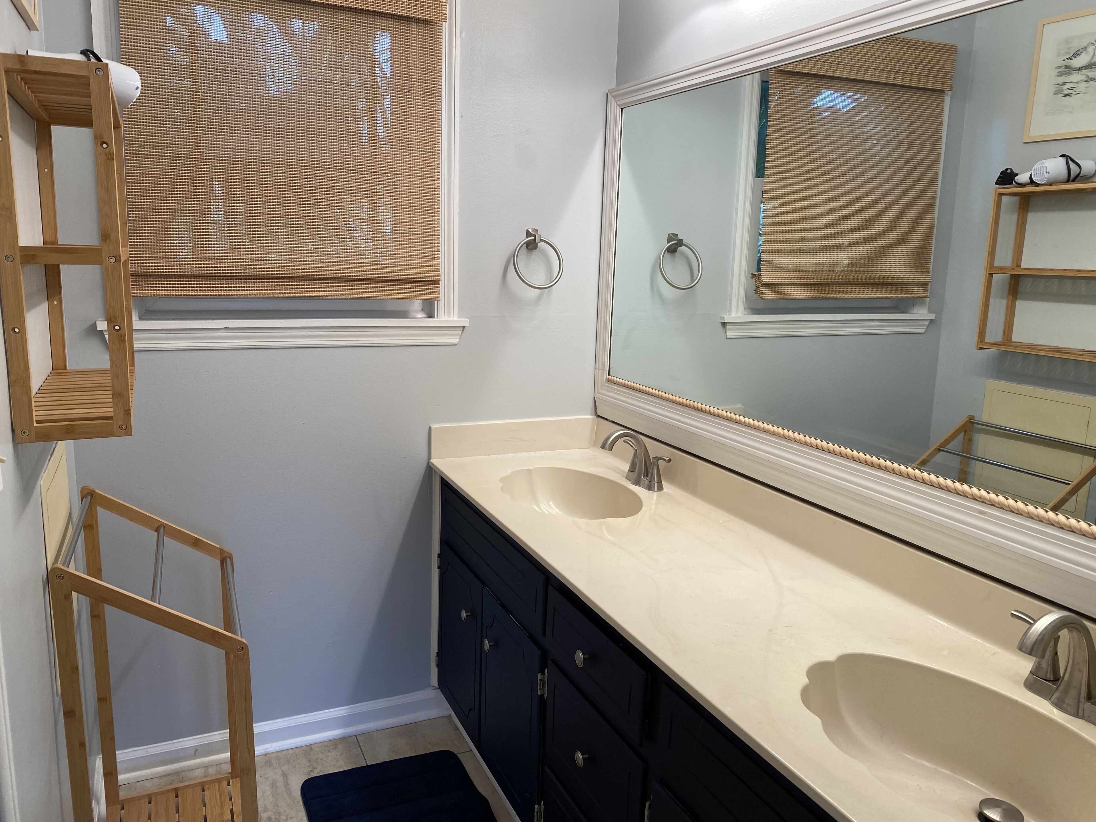A bathroom with a double sink, a large mirror, a wooden ladder, and a window with a bamboo blind.