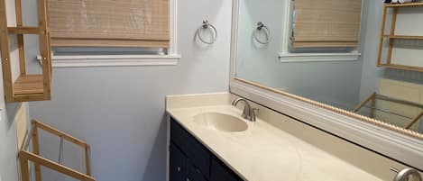 A bathroom with a double sink, a large mirror, a wooden ladder, and a window with a bamboo blind.