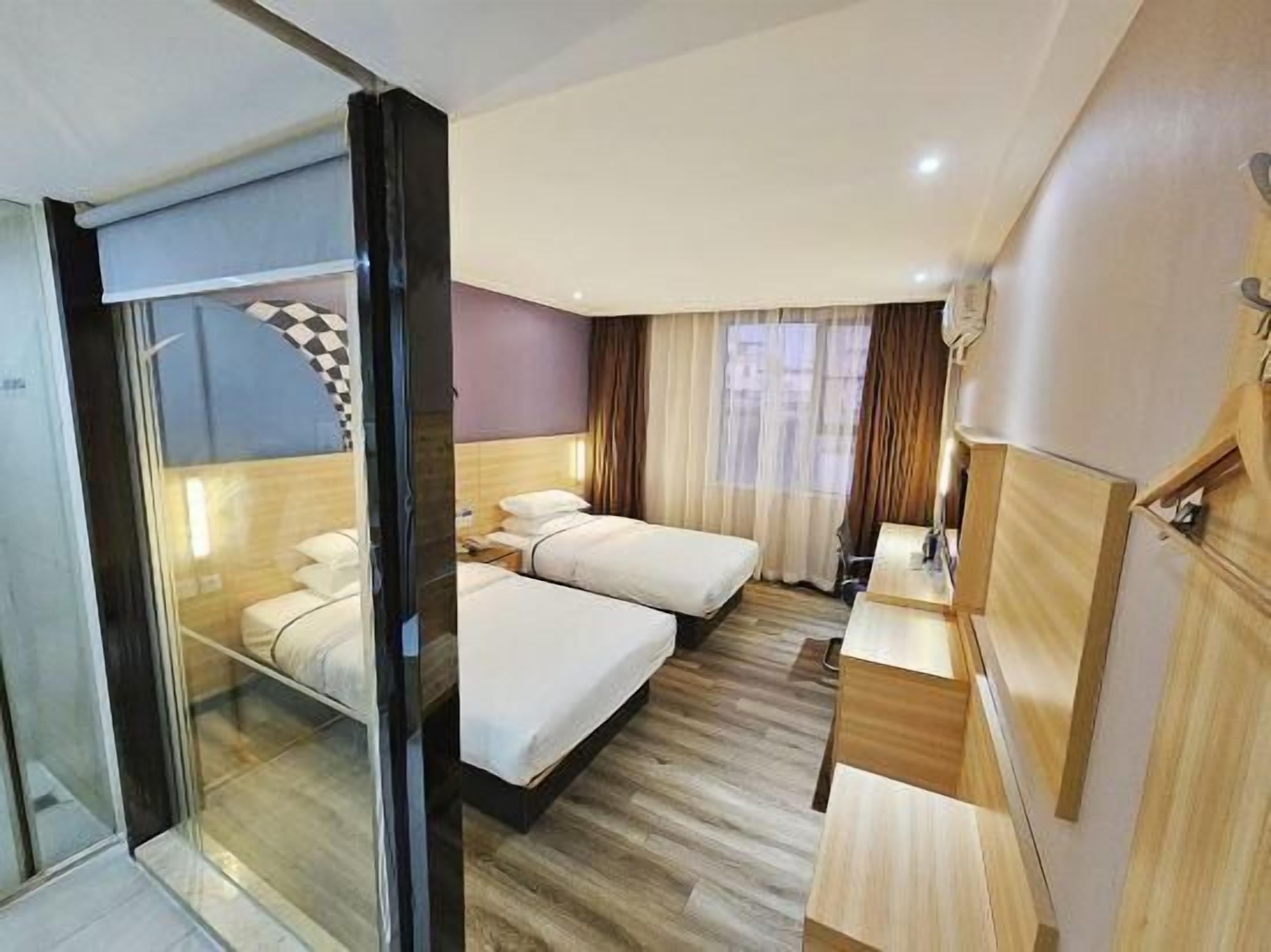 Habitación de hotel con dos camas, un separador de vidrio, un escritorio y un espejo.