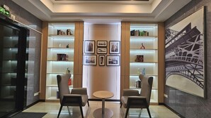 Un hall d’entrée moderne avec deux fauteuils, une petite table ronde et des étagères remplies de livres et ornées de tableaux encadrés.