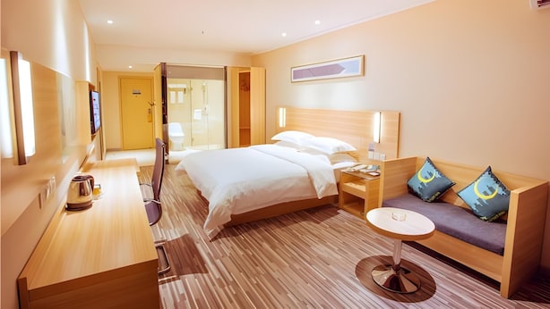 Une chambre d’hôtel avec un lit, une table de chevet, une petite table ronde, un canapé avec des coussins, une télévision et un plancher en bois.