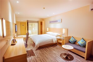 Une chambre d’hôtel avec un lit, une table de chevet, une petite table ronde, un canapé avec des coussins, une télévision et un plancher en bois.