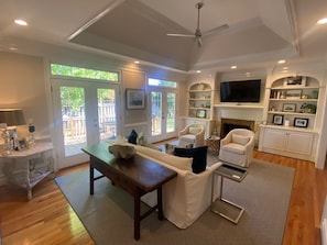 A spacious living room with a wooden floor, a large window, a fireplace, and a television. - Gated Golf Community - West Lake - Master's Rental (Martinez)