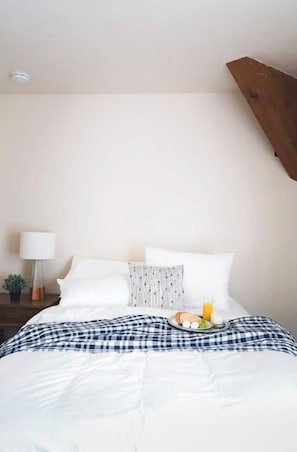 A neatly made bed with a checkered blanket, pillows, and a plate of breakfast.