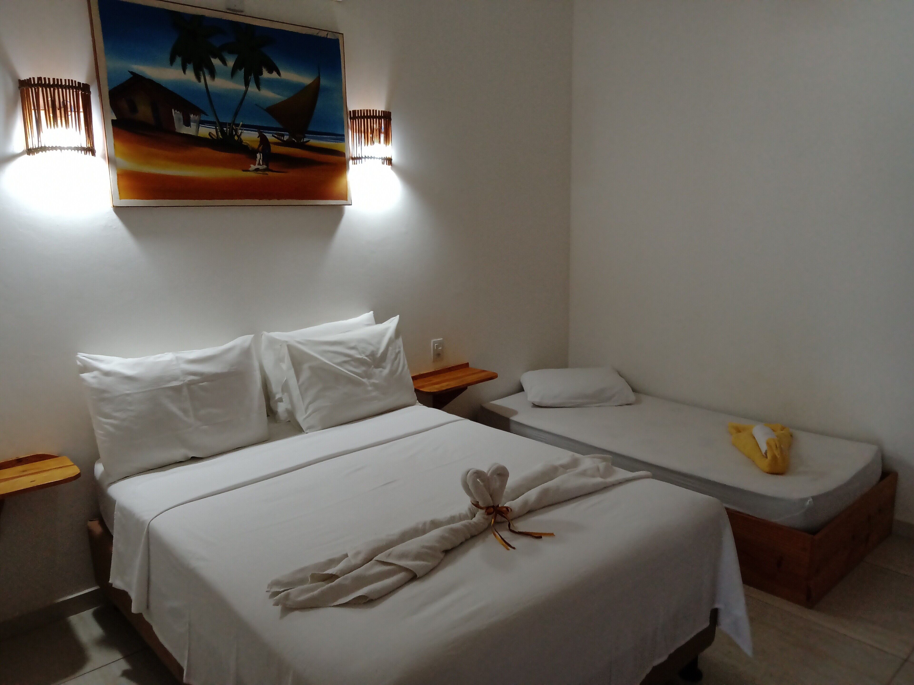 A hotel room with a large bed, a smaller bed, a painting on the wall, and a nightstand with a lamp.