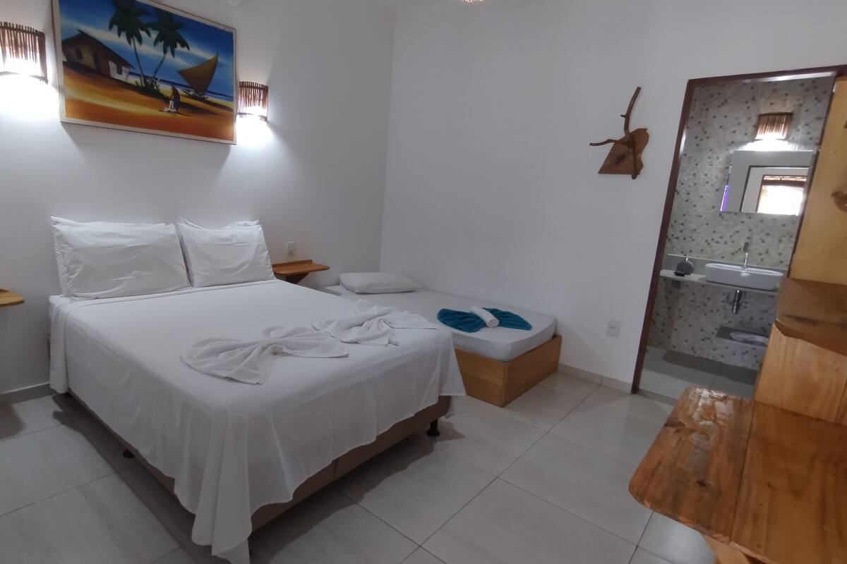 Ein Hotelzimmer mit einem Bett, einem kleinen Nachttisch, einer Ablage, einer Holzbank, einem Spiegel und einem durch eine offene Tür einsehbaren Badezimmer.