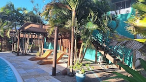 A poolside area with a wooden deck, palm trees, and a covered seating area. - Hawaii Flats (São Miguel do Gostoso)