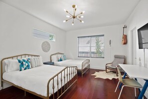 Une chambre avec deux lits, un bureau, une chaise, une guitare et une fenêtre avec des stores.