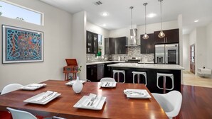 A modern kitchen with a central island, dark cabinetry, and pendant lighting. - DwellHTX Modern Designer Home 1 mi frm Downtown 2-Story Getaway w/ Views (Houston)
